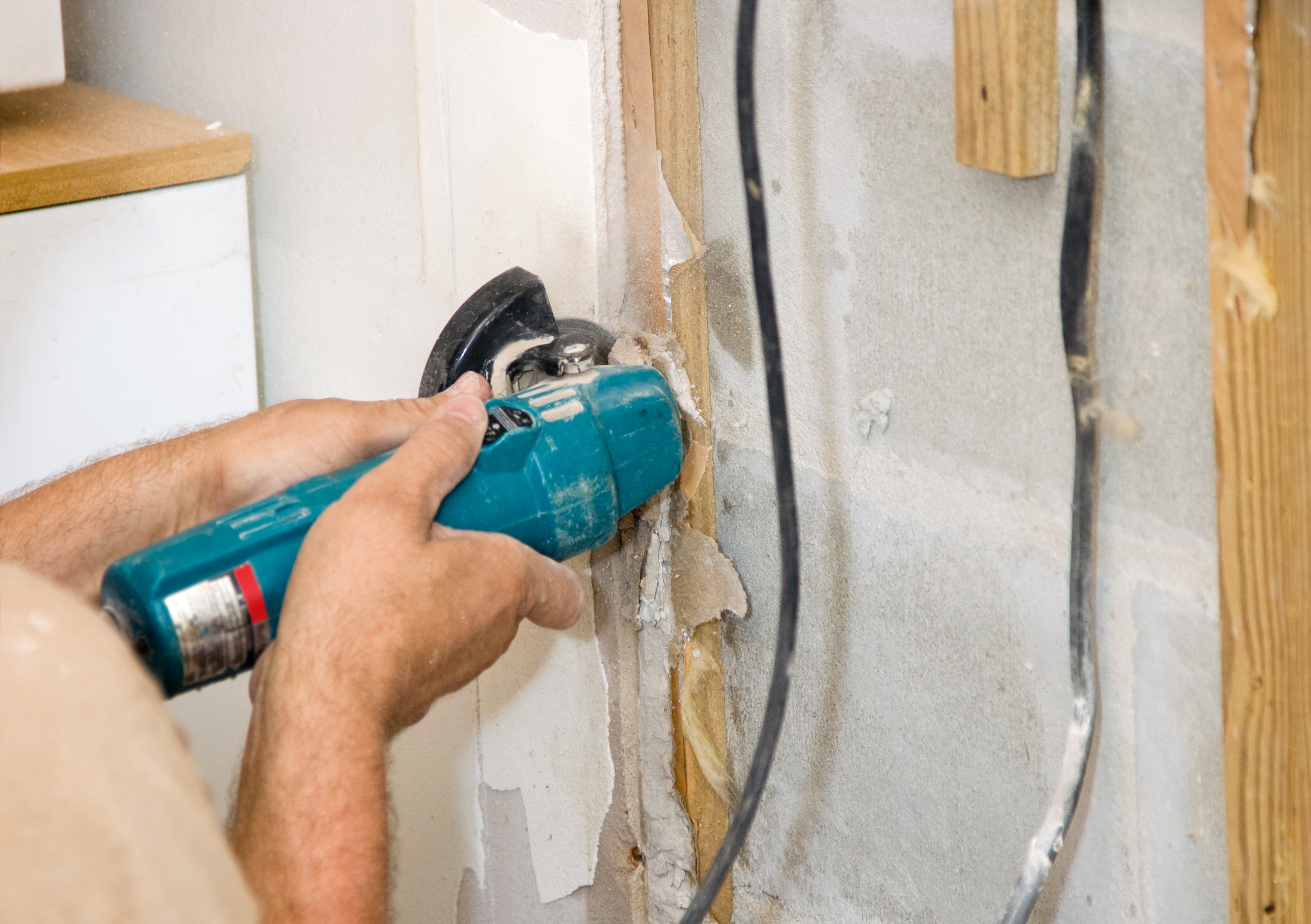 Contractor using an angle grinder to cut through a section of drywall, producing sparks and fine dust as the tool's rotating disc makes contact with the wall material. Contractor using an angle grinder to cut through a section of drywall, producing sparks and fine dust as the tool's rotating disc makes contact with the wall material.