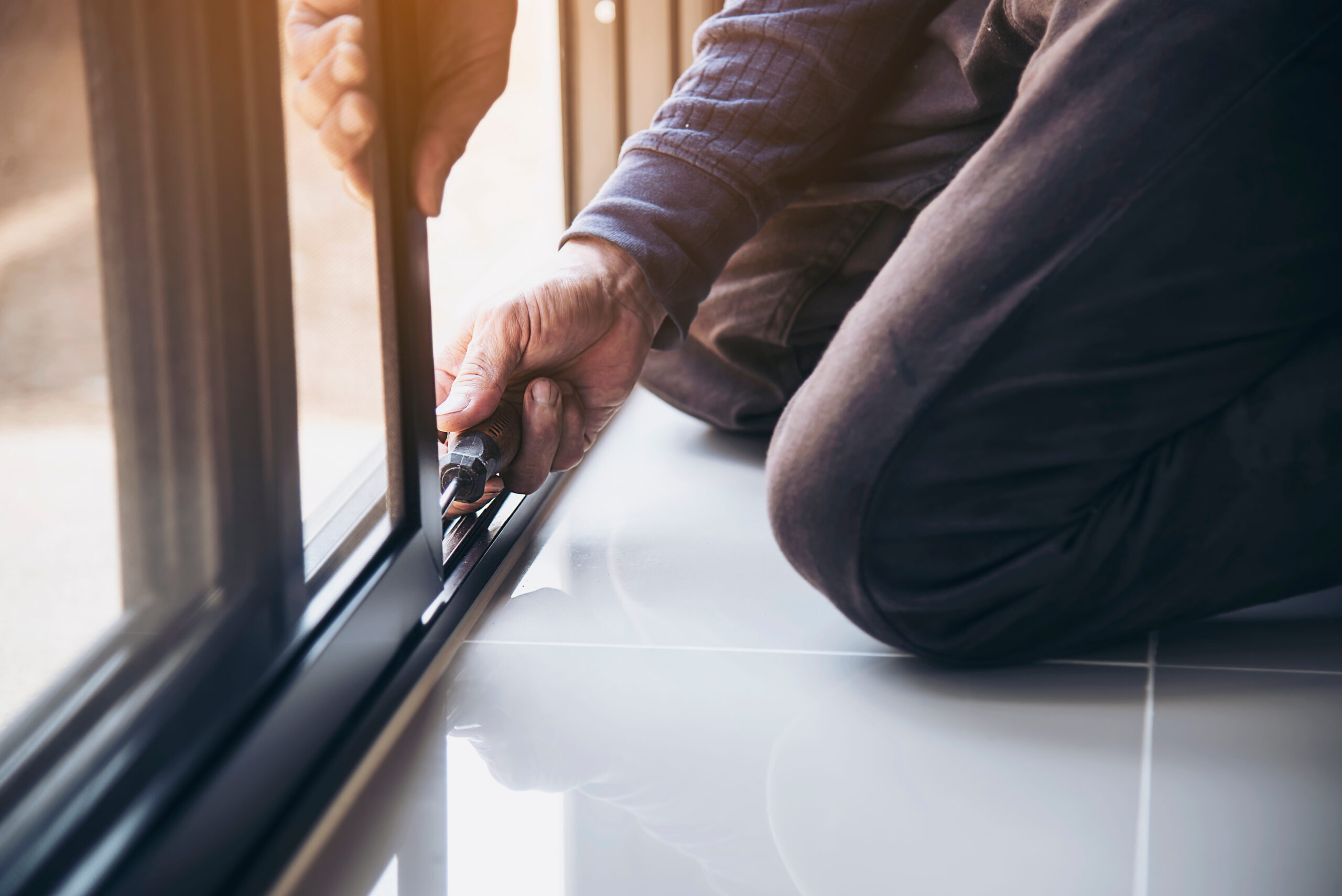 A skilled construction worker wearing safety glasses carefully assembling an aluminum frame for a window installation at a construction site. A skilled construction worker wearing safety glasses carefully assembling an aluminum frame for a window installation at a construction site.