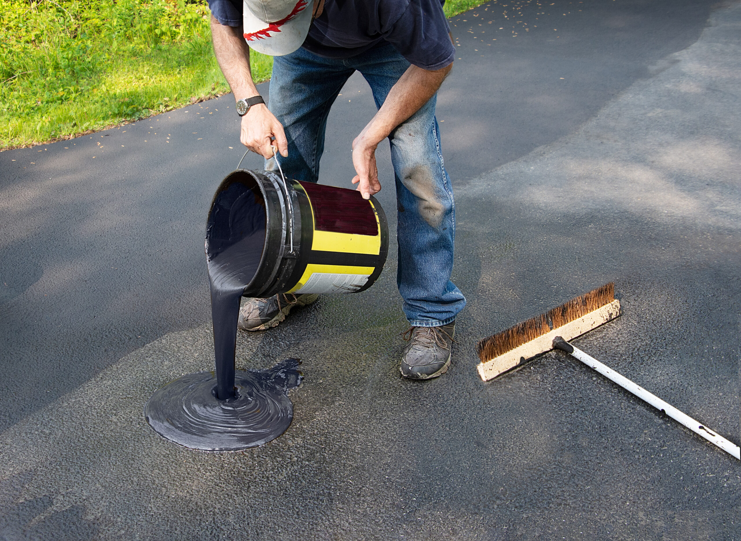 Worker pouring freshly heated asphalt onto a driveway as part of the resealing process.
